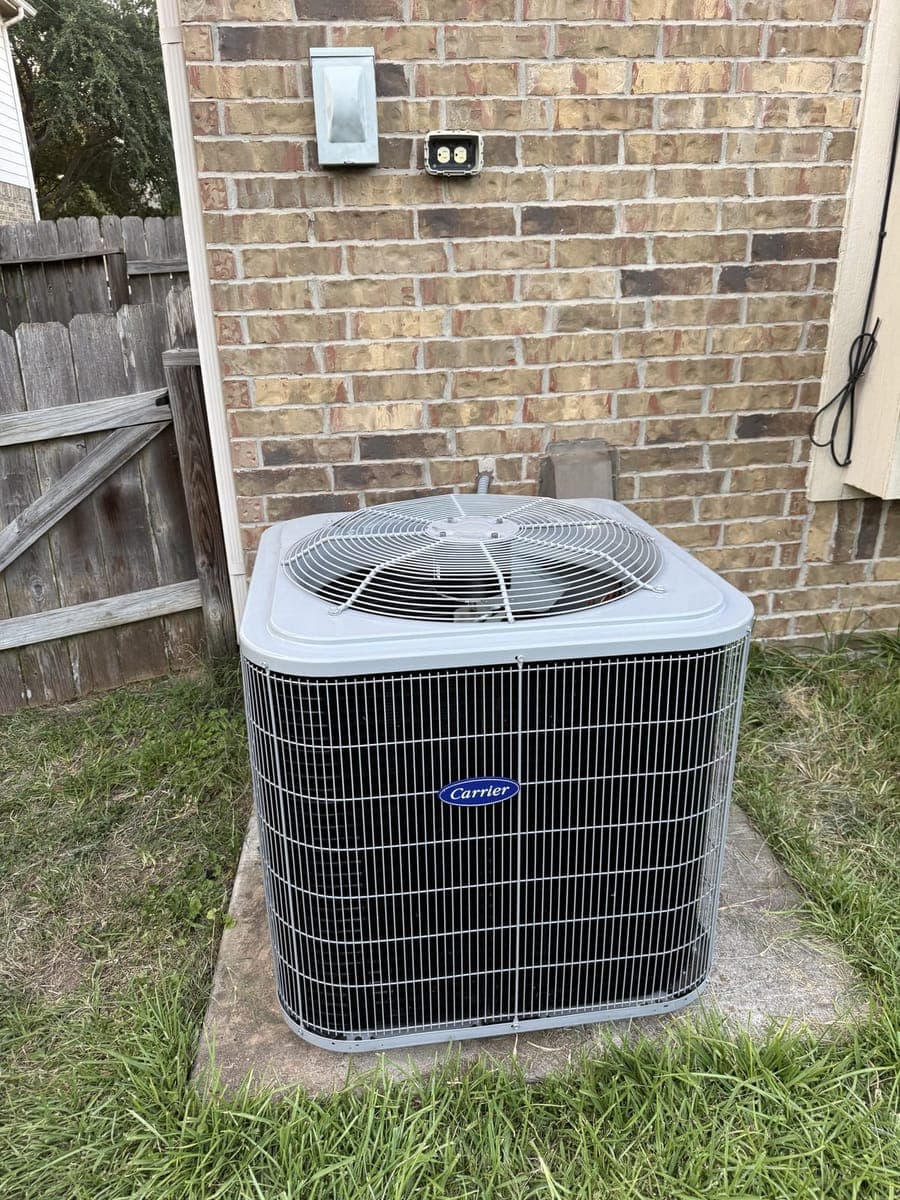 New Carrier outdoor condenser on a pad beside a brick house