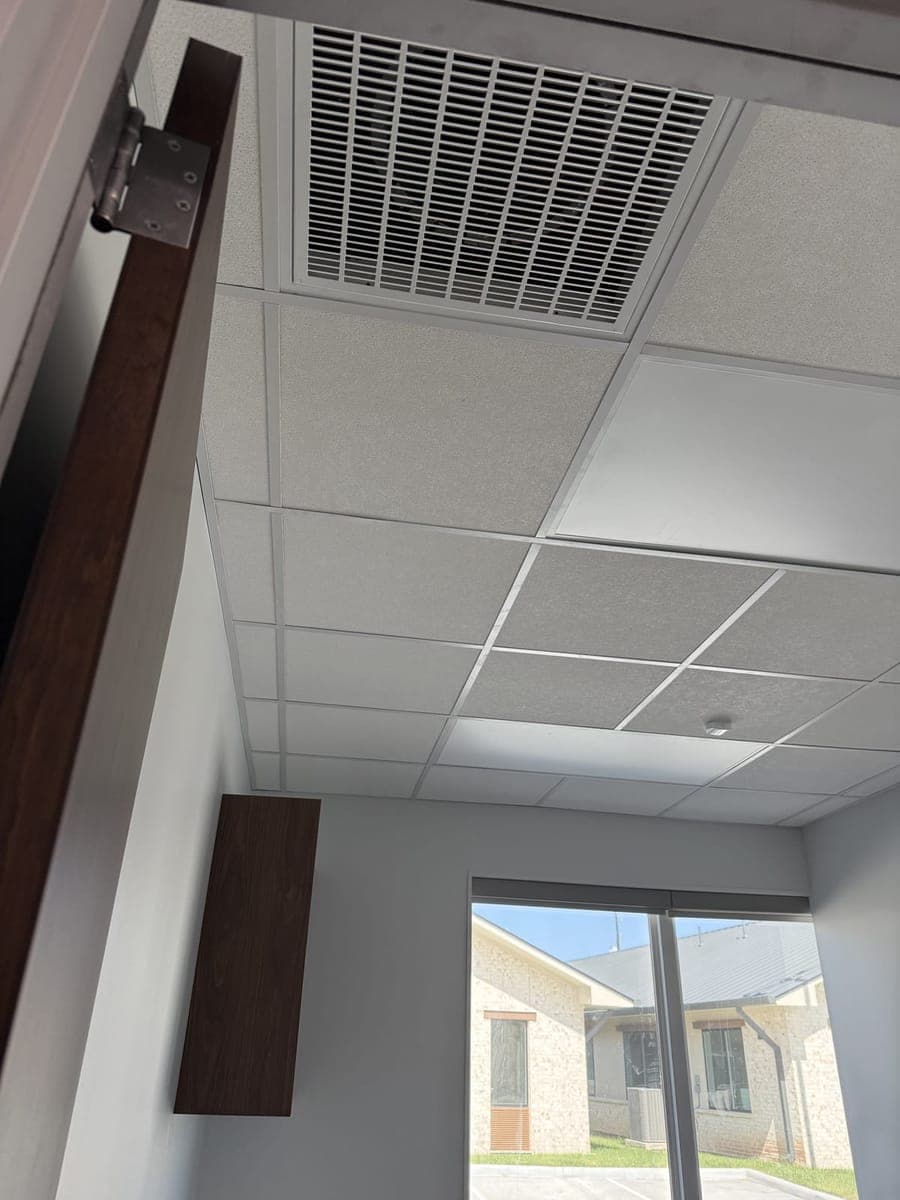 Return air grille in an office drop ceiling near a window