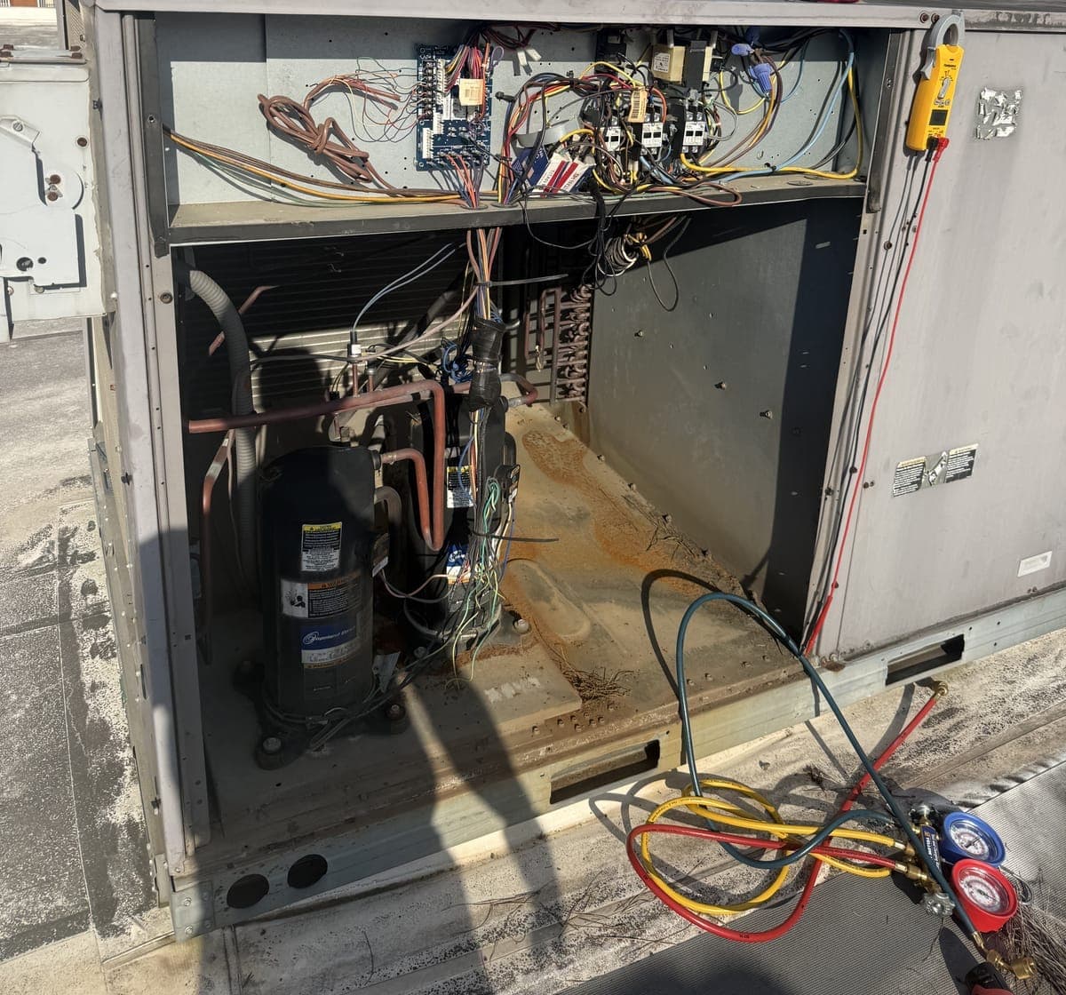 Rooftop package unit with its panels removed, showing the compressor, controls, and gauges connected