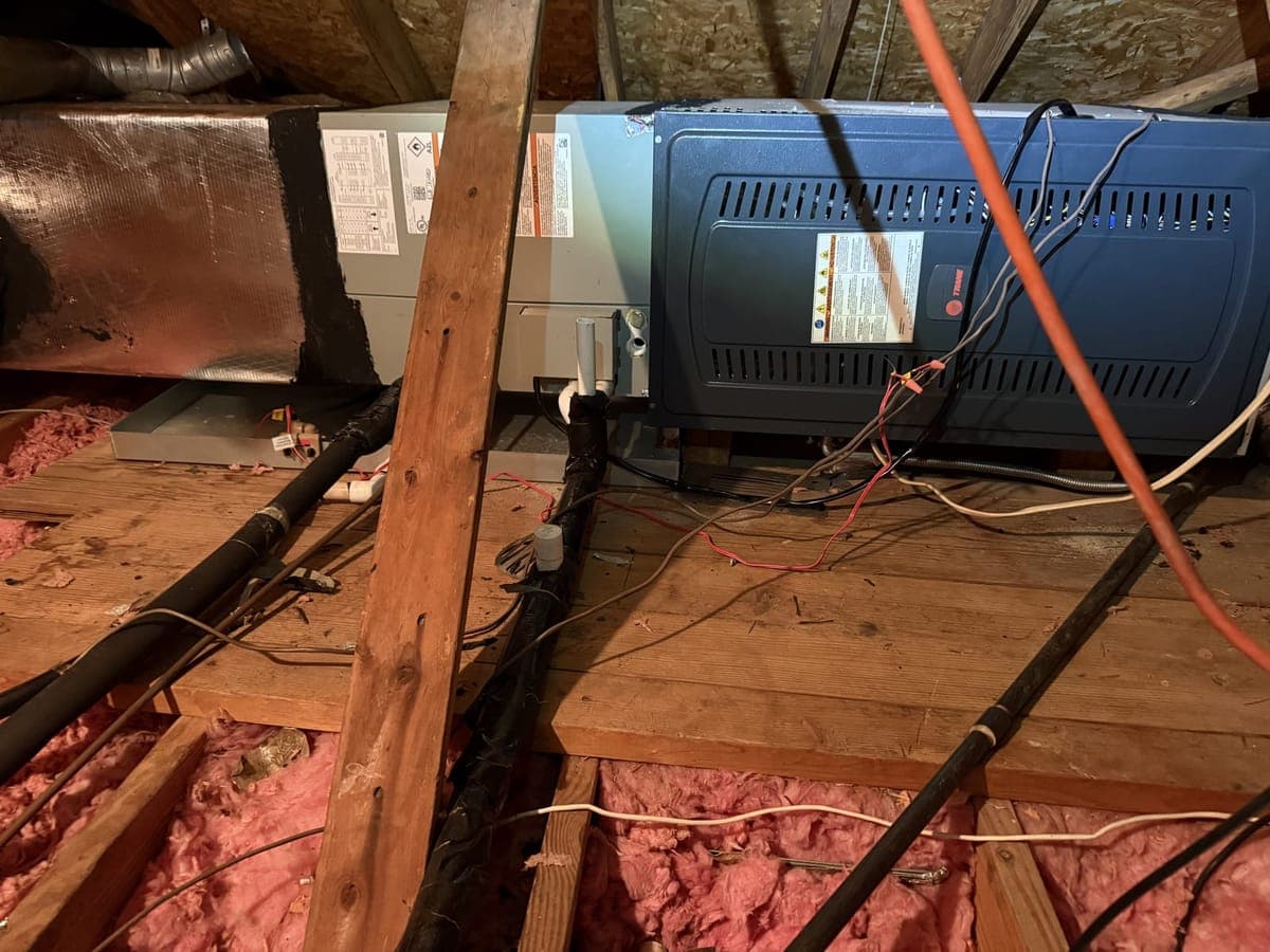 New blue Trane indoor unit on a platform in an attic, with wiring and refrigerant lines connected